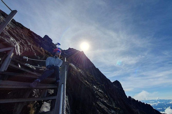Wooden steps and a fixed rope on the Mount Kinabalu summit trail, with the sun breaking over the ridge